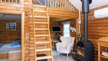 A log cabin interior with a wooden ladder, a white armchair, a fireplace, and a television.