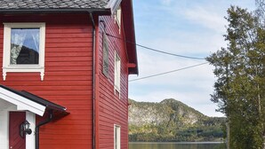 A red wooden house with a dock leading to a lake, surrounded by trees and hills. - Holiday Home in MÃ¥ndalen (Rauma)