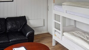 A bunk bed with white bedding, a black leather sofa, and a round wooden table with a book. - Holiday Home in MÃ¥ndalen (Rauma)