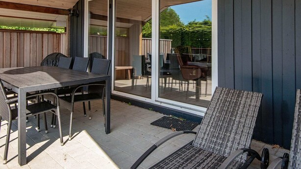 A covered patio area with a table and chairs, a sliding glass door leading to an outdoor space, and a wooden ceiling. - 8 Person Holiday Home in Hejls-by Traum (Hejls)