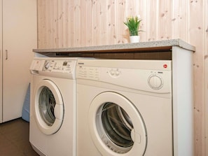 Compact laundry room with modern design, featuring a bathtub, laundry machines, and a small potted plant.