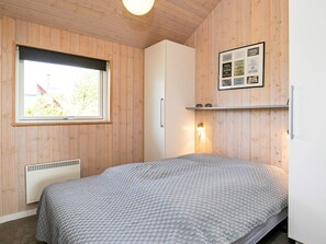 A bedroom with a bed, a window, a wall-mounted shelf, and a framed picture.