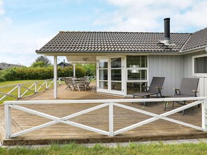 A house with a covered deck, a chimney, and a glass door leading to a patio area with outdoor furniture.