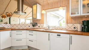 A modern kitchen with white cabinets, a stainless steel range hood, and a window providing natural light. - 5 Star Holiday Home in Lemvig (Lemvig)