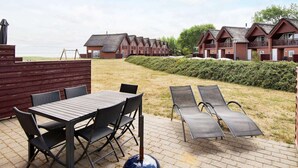 A patio area with a table and chairs, lounge chairs, and a view of a row of brick houses with balconies. - Luxury Retreat With Sea View - By Traum Ferienwohnungen (Rømø)