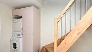 A laundry area with stacked appliances and a wooden staircase. - Luxury Retreat With Sea View - By Traum Ferienwohnungen (Rømø)