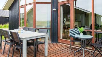 Un patio exterior con una mesa y sillas, una mesa redonda con una planta y un amplio ventanal que da a un espacio interior.
