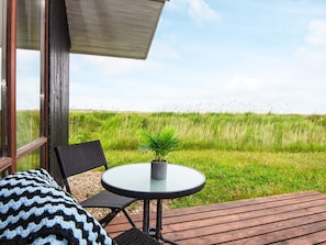 A wooden deck with a round table and two chairs, overlooking a grassy field. - 5 Star Holiday Home in Ulfborg (Ulfborg)