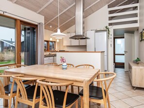 A modern kitchen with wooden cabinets, a dining table with chairs, and pendant lighting.