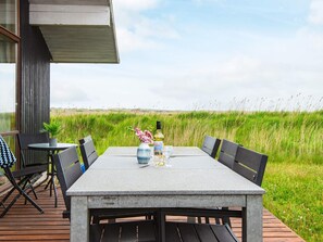 An outdoor dining area with a table and chairs, a potted plant, and a bottle of wine. - 5 Star Holiday Home in Ulfborg (Ulfborg)
