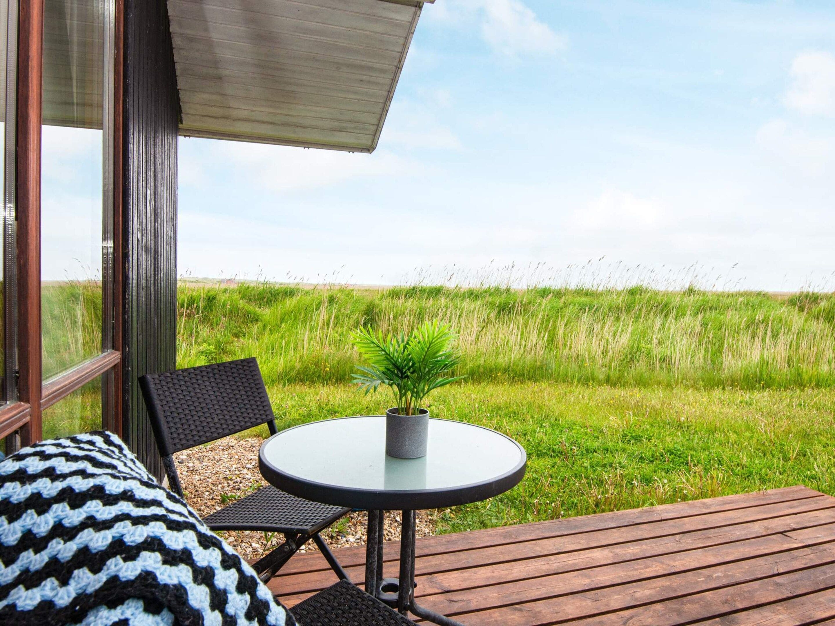 A deck with a round table and chairs, a potted plant, and a view of a grassy field.