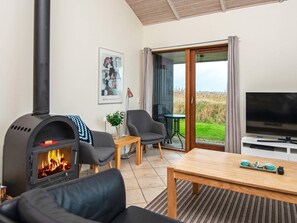 A living room with a fireplace, a sofa, a television, and a view of the outdoors. - 5 Star Holiday Home in Ulfborg (Ulfborg)