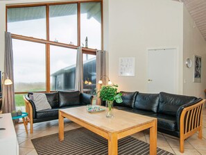 A living room with a black leather sofa, a wooden coffee table, and a large window with curtains.