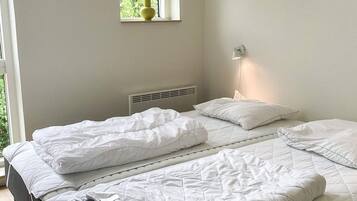 A bedroom with two beds, a window with a plant, a wall-mounted light, and a radiator.