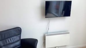 A black leather sofa, a wall-mounted TV, and a white radiator in a room with wooden flooring. - 4 Star Holiday Home in Vaeggerlose (Vaeggerlose)