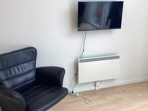 A black leather sofa, a wall-mounted TV, and a white radiator in a room with wooden flooring. - 4 Star Holiday Home in Vaeggerlose (Vaeggerlose)