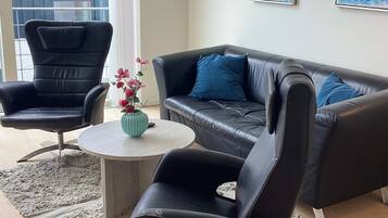 A modern living room with a black leather sofa, two black leather armchairs, a round coffee table, and a vase with flowers.
