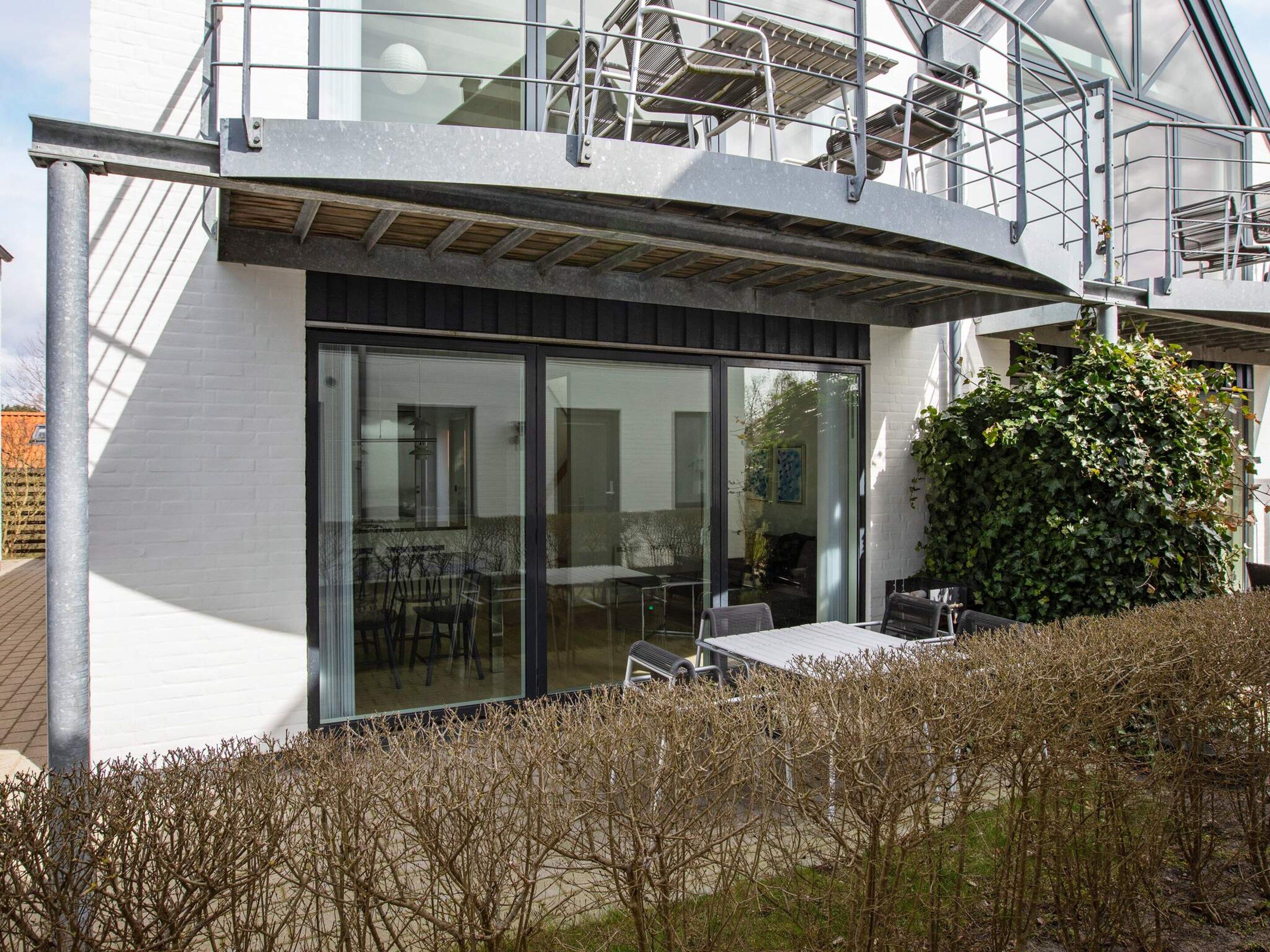 A modern building with a glass facade, outdoor seating area, and a staircase leading to an upper level.