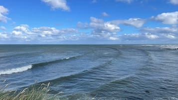 Vista costera con olas, cielo despejado y algunas nubes.