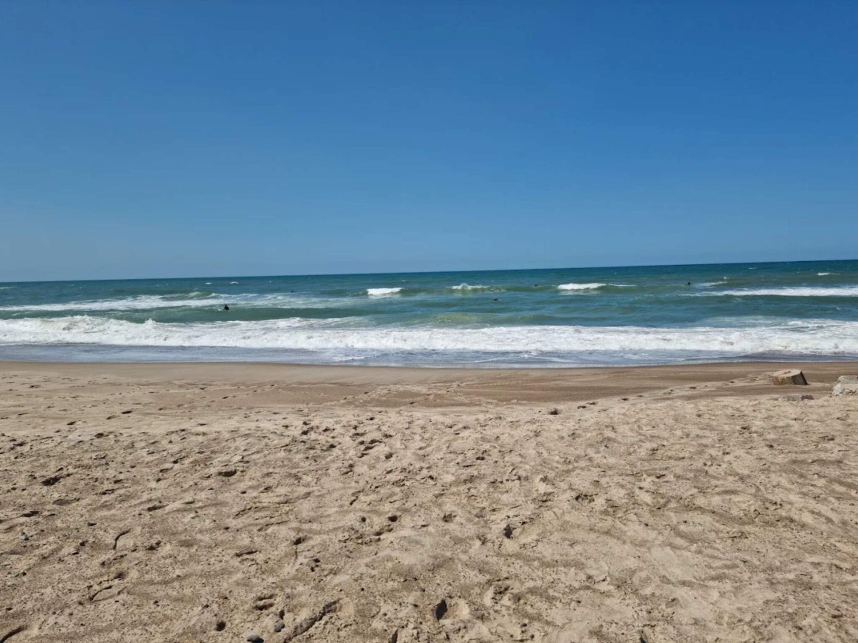 A sandy beach with waves, clear sky, and no visible structures.