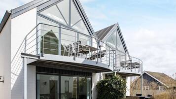 A modern two-story house with large glass windows, a balcony with metal railings, and a well-maintained garden.