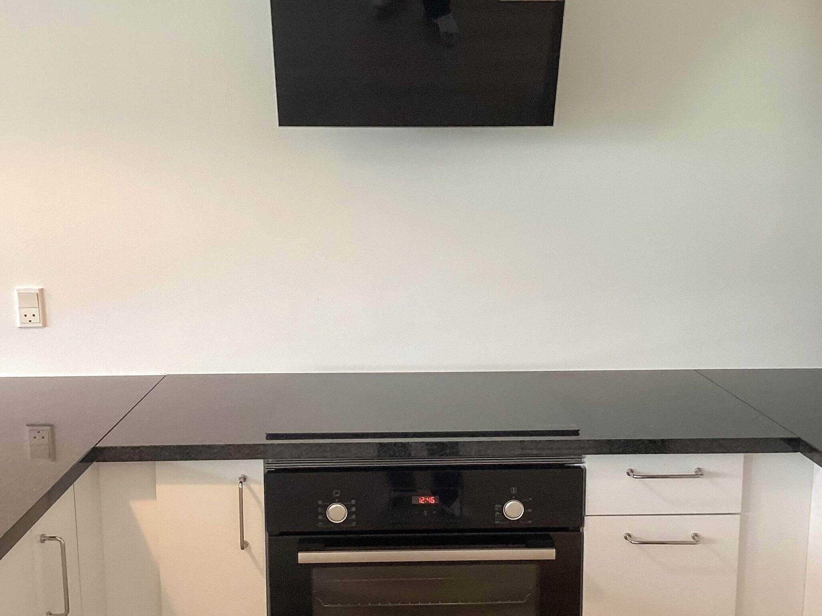 Una cocina con estufa negra, armarios blancos y encimera negra.