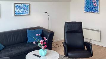 A modern living room with a black leather sofa, a round coffee table with a vase of flowers, a black office chair, and a standing lamp.