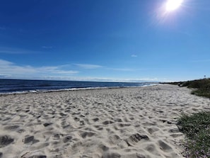 A sandy beach with footprints, a clear sky, and the ocean.