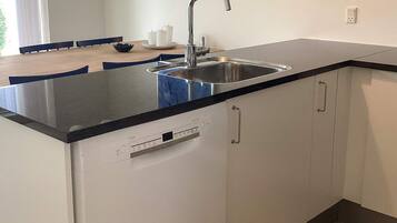 A kitchen with a stainless steel sink, white cabinets, and a black countertop.