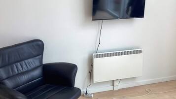 A black leather sofa, a wall-mounted TV, and a white radiator in a room with wooden flooring.