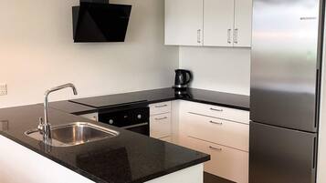 A modern kitchen with a stainless steel refrigerator, a black countertop, and white cabinets.
