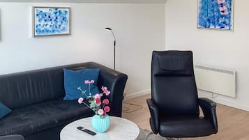 A modern living room with a black leather sofa, a round coffee table with a vase of flowers, a black leather armchair, and two abstract paintings on the walls.