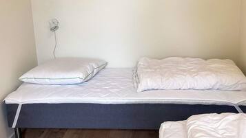 A single bed with white bedding, a pillow, and a bedside table with a lamp.