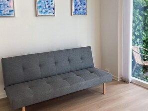 En grå soffa i ett rum med ett fönster och tre inramade konstverk på väggen.