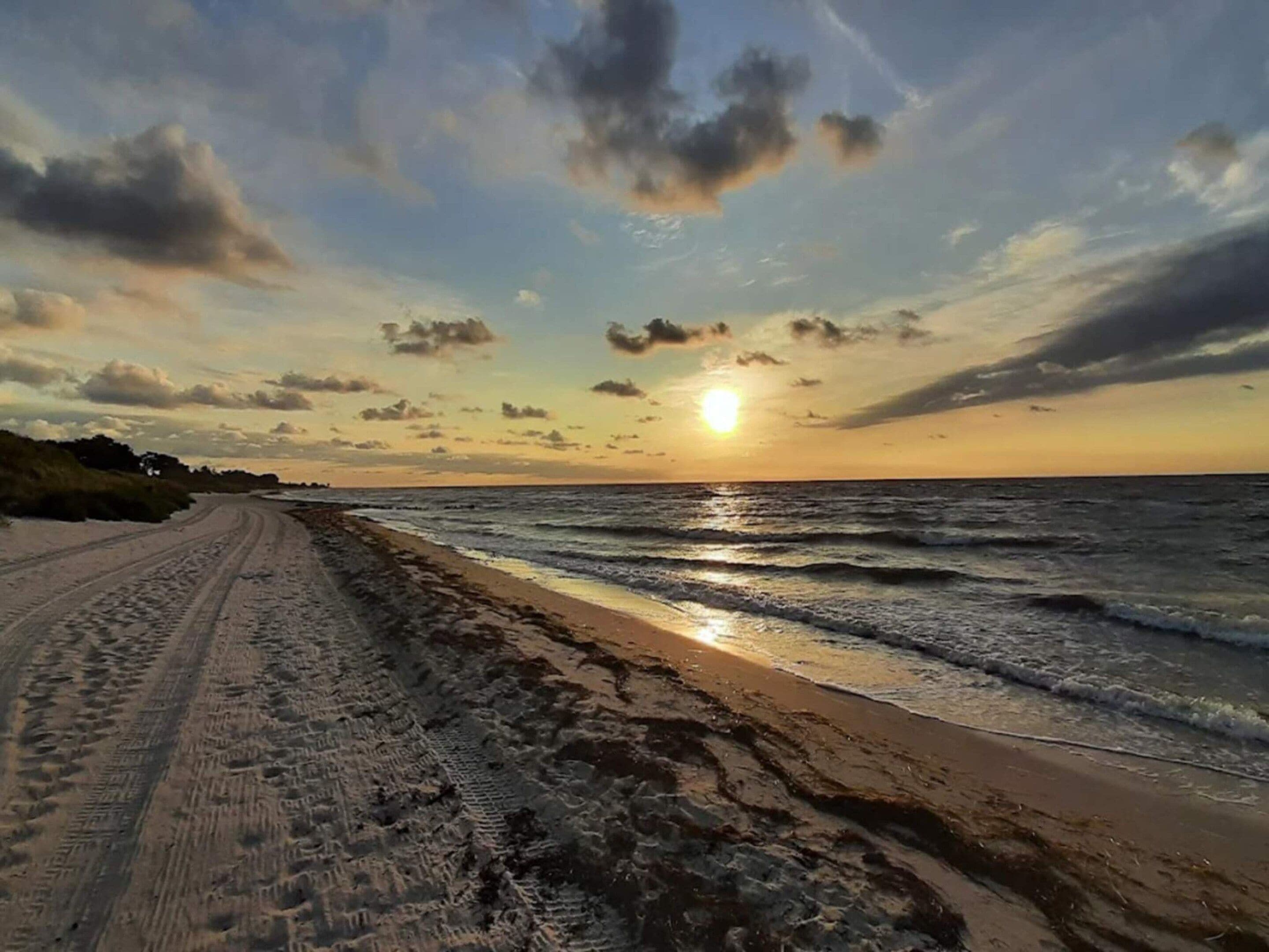 A beach with a clear sky and the sun setting over the horizon.