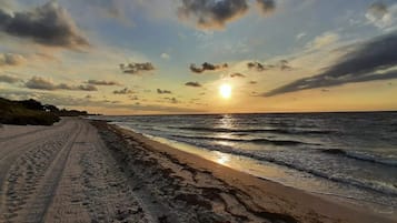 A beach with a clear sky and the sun setting over the horizon.