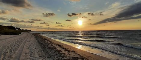 A beach with a clear sky and the sun setting over the horizon.