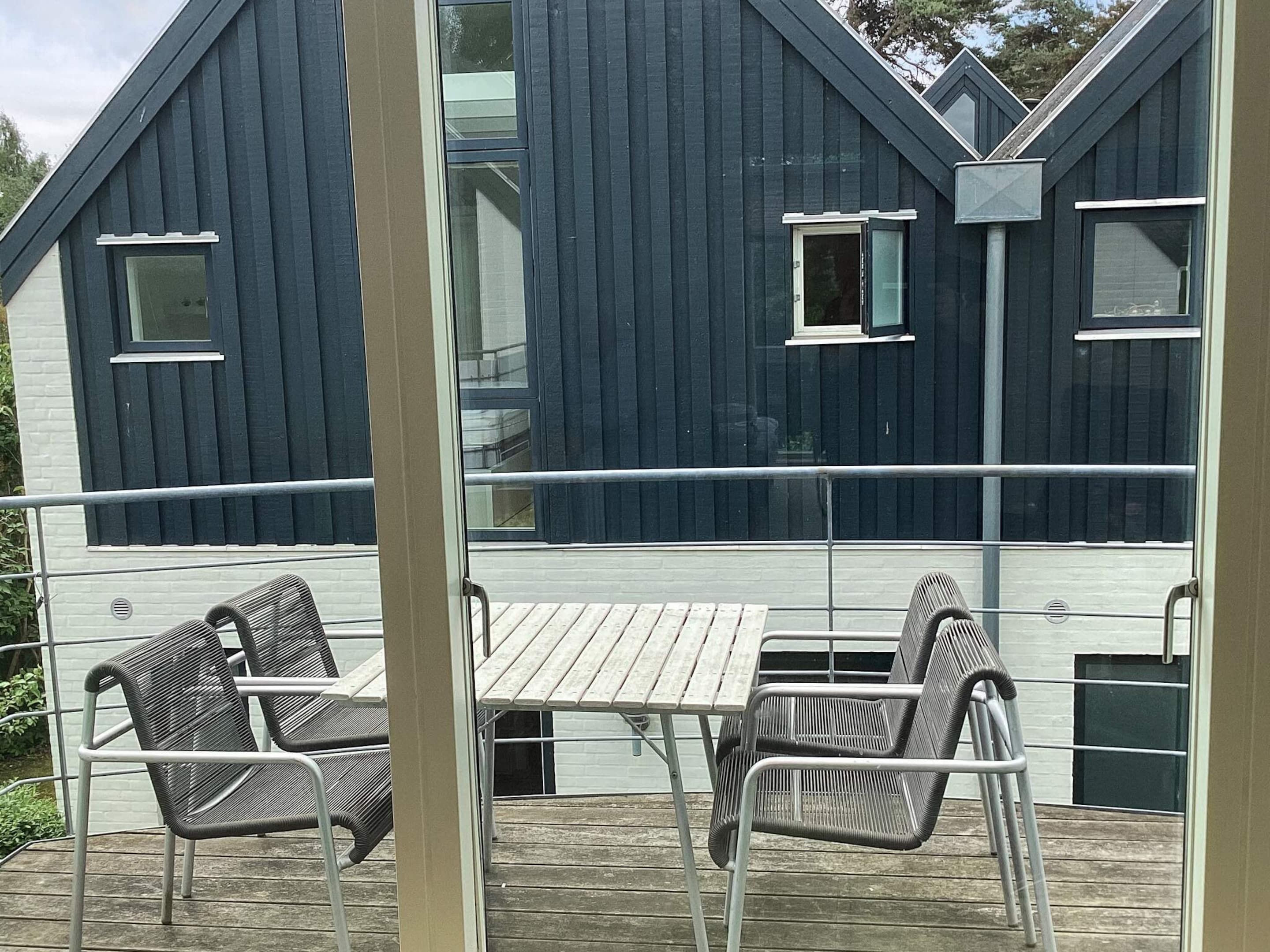 A wooden deck with metal chairs and a table, overlooking a dark blue building with white trim and multiple windows.