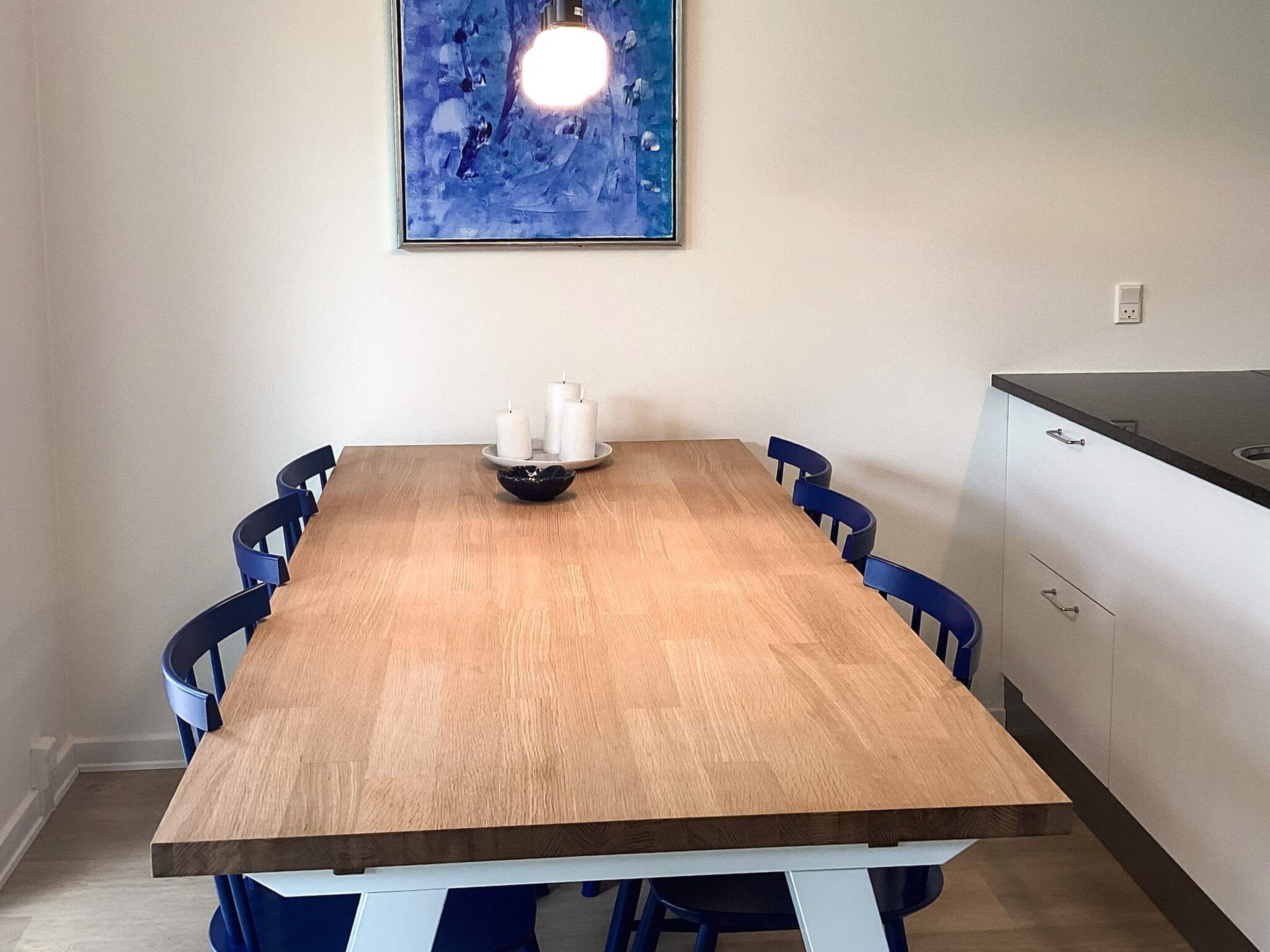 A dining room with a wooden table, six blue chairs, a white candle holder, and a blue abstract painting on the wall.