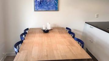 A dining room with a wooden table, six blue chairs, a white candle holder, and a blue abstract painting on the wall.
