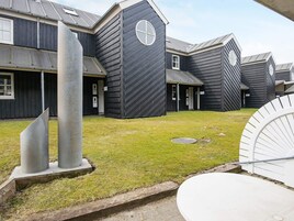 Un edificio con fachada oscura, un patio con césped y una estructura metálica en primer plano.