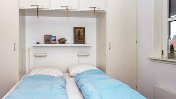 Un dormitorio con cama, armario, estante con objetos y ventana.