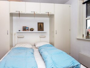 Et soveværelse med seng, skab, en hylde med ting og et vindue.