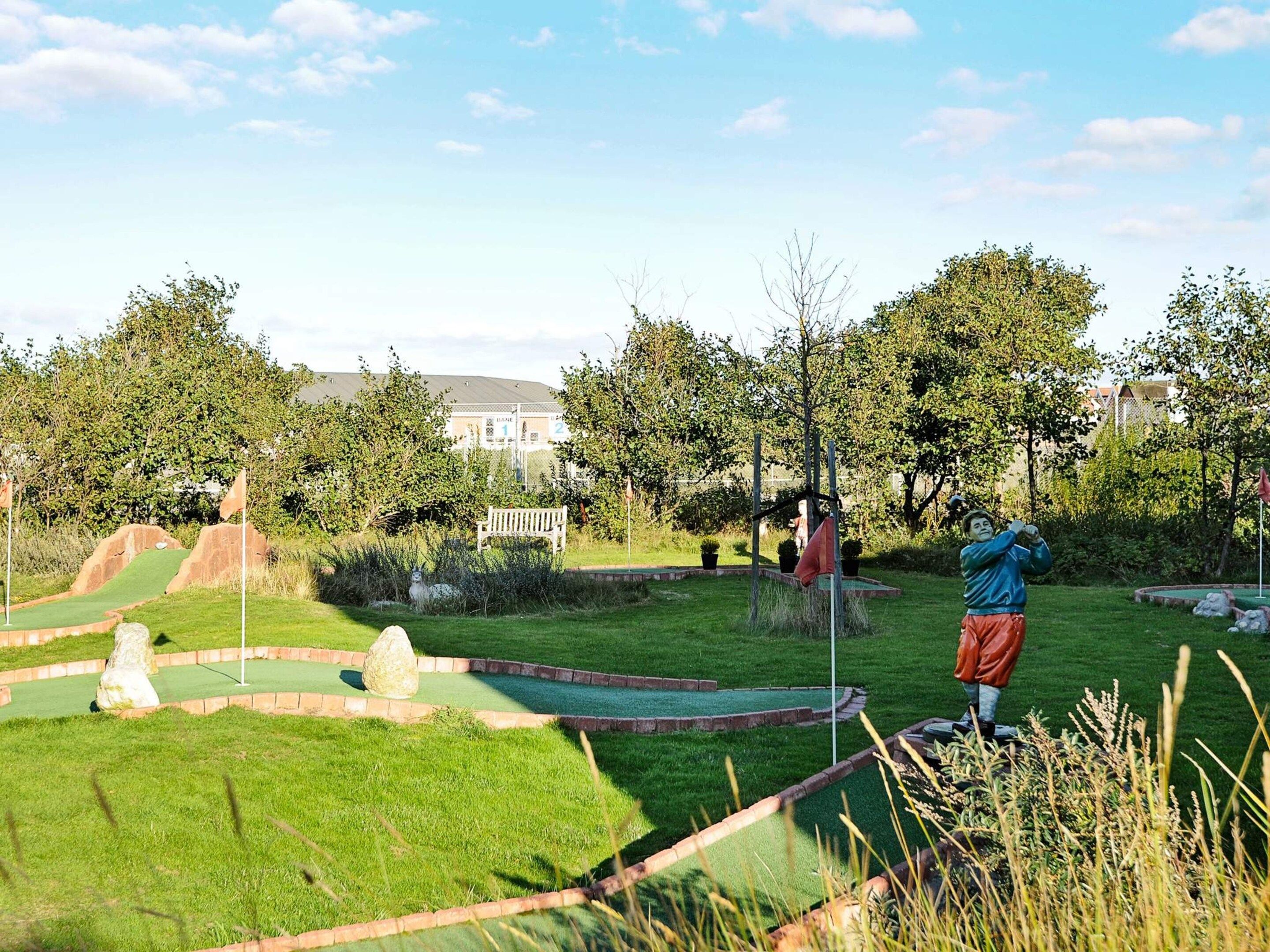 A miniature golf course with a statue of a golfer, a flag, and a bench.