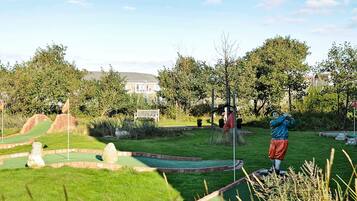 A miniature golf course with a statue of a golfer, a flag, and a bench.