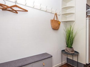 A room with a white wall, a grey bench, a hanging basket, and a potted plant.