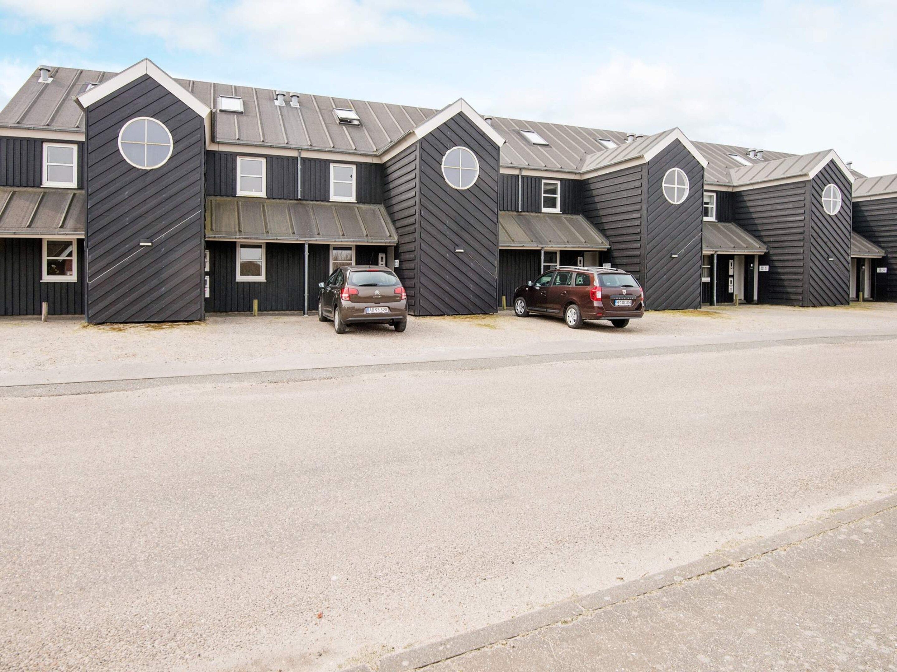 A row of identical buildings with a garage door entrance, a parking lot, and two cars parked in front.
