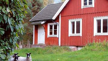 A red house with white trim and multiple windows, surrounded by green grass and trees.