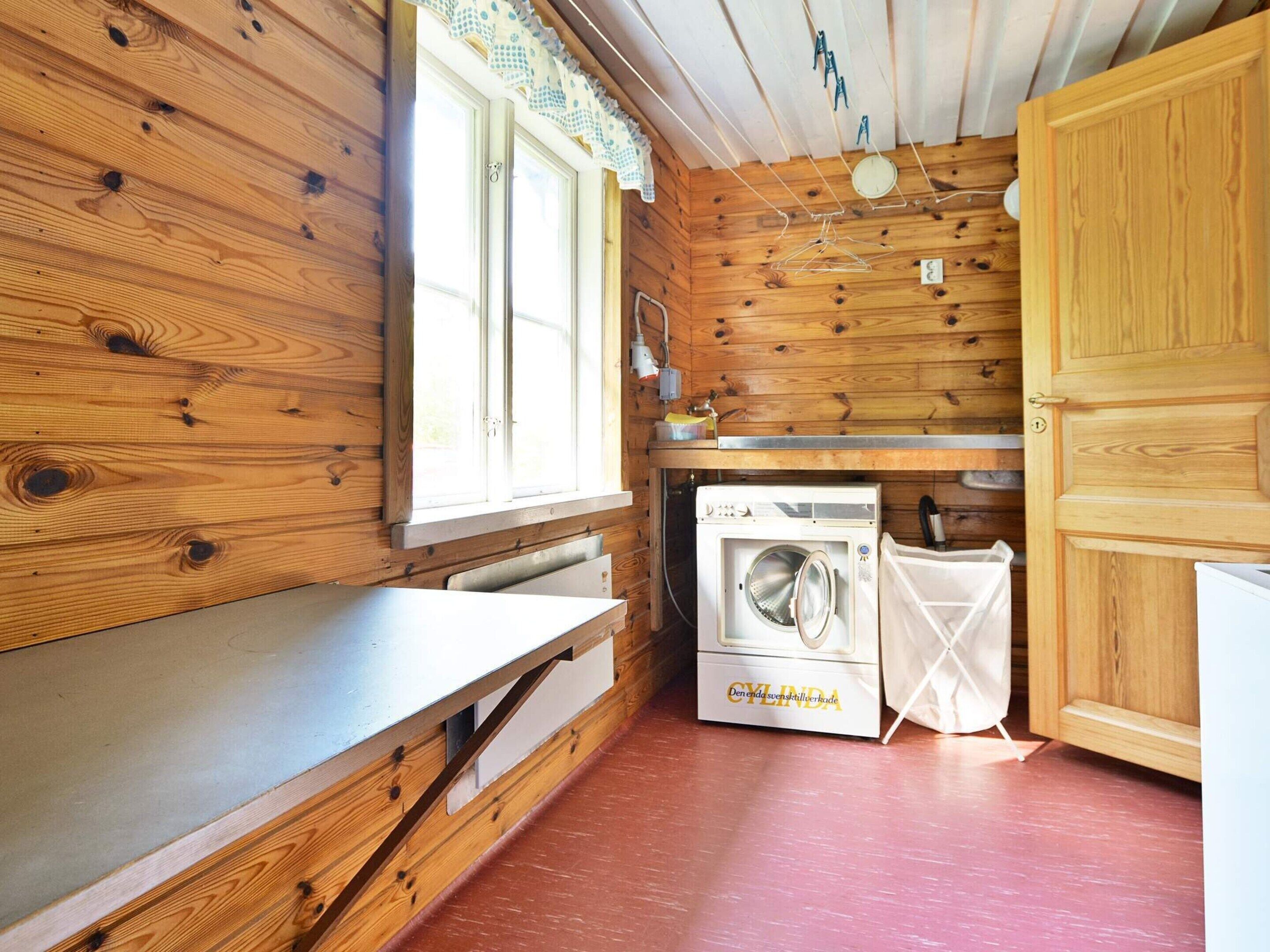 L’intérieur d’une cabane en bois, avec un lave-linge, un évier et une fenêtre avec des rideaux.