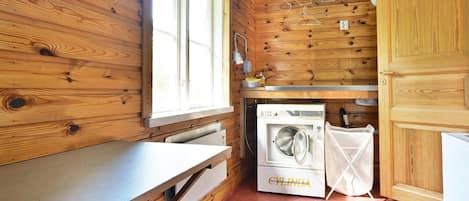 L’intérieur d’une cabane en bois, avec un lave-linge, un évier et une fenêtre avec des rideaux.